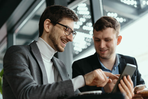 One-on-one meeting. Two young business people sitting at table in restaurant having a conversation using a phone and having a coffee. Businessman using a smartphone